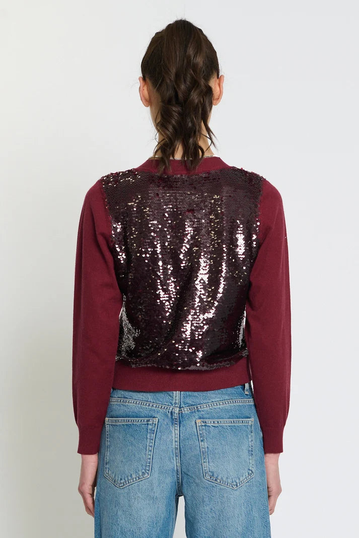 A model viewed from the back wearing a long-sleeve crop top with a burgundy base and a large, dark sequined back panel, paired with blue jeans against a plain white background.