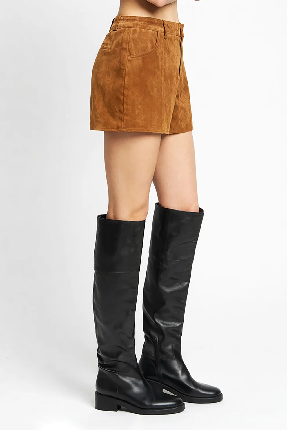 A model from the waist down wearing brown suede shorts and black knee-high leather boots, photographed against a clean white studio background.