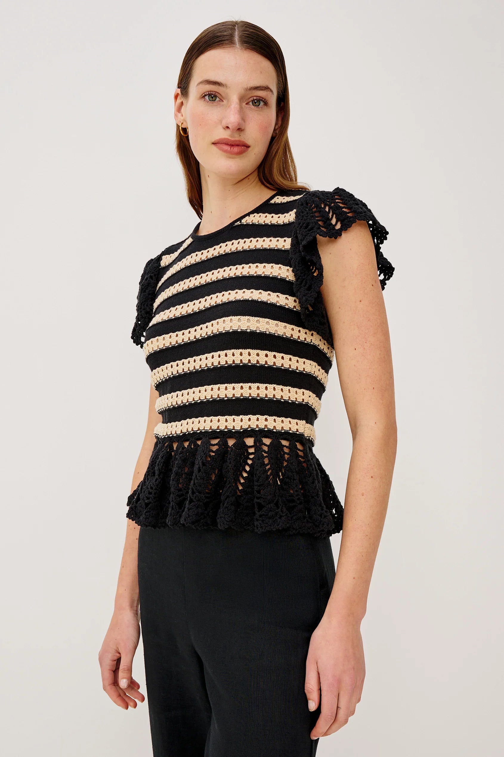 Woman wearing a black and beige striped top with ruffled details on a white background