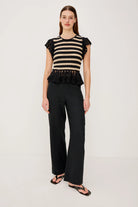 Woman wearing a black and beige striped top with ruffled details and black pants on a white background