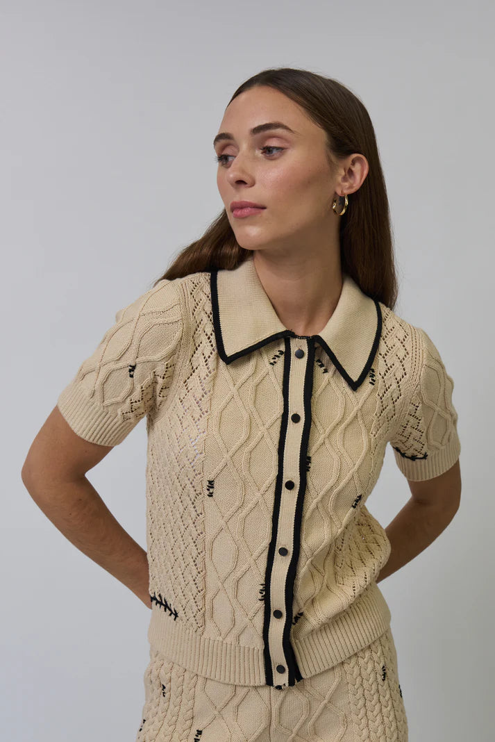 Woman wearing a beige cable knit cardigan with black trim on a plain background