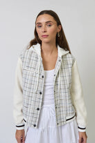 Woman wearing a plaid jacket over a white top and skirt on a plain background