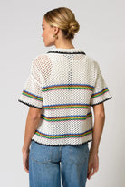 Person wearing a white knit top with rainbow trim on a plain background