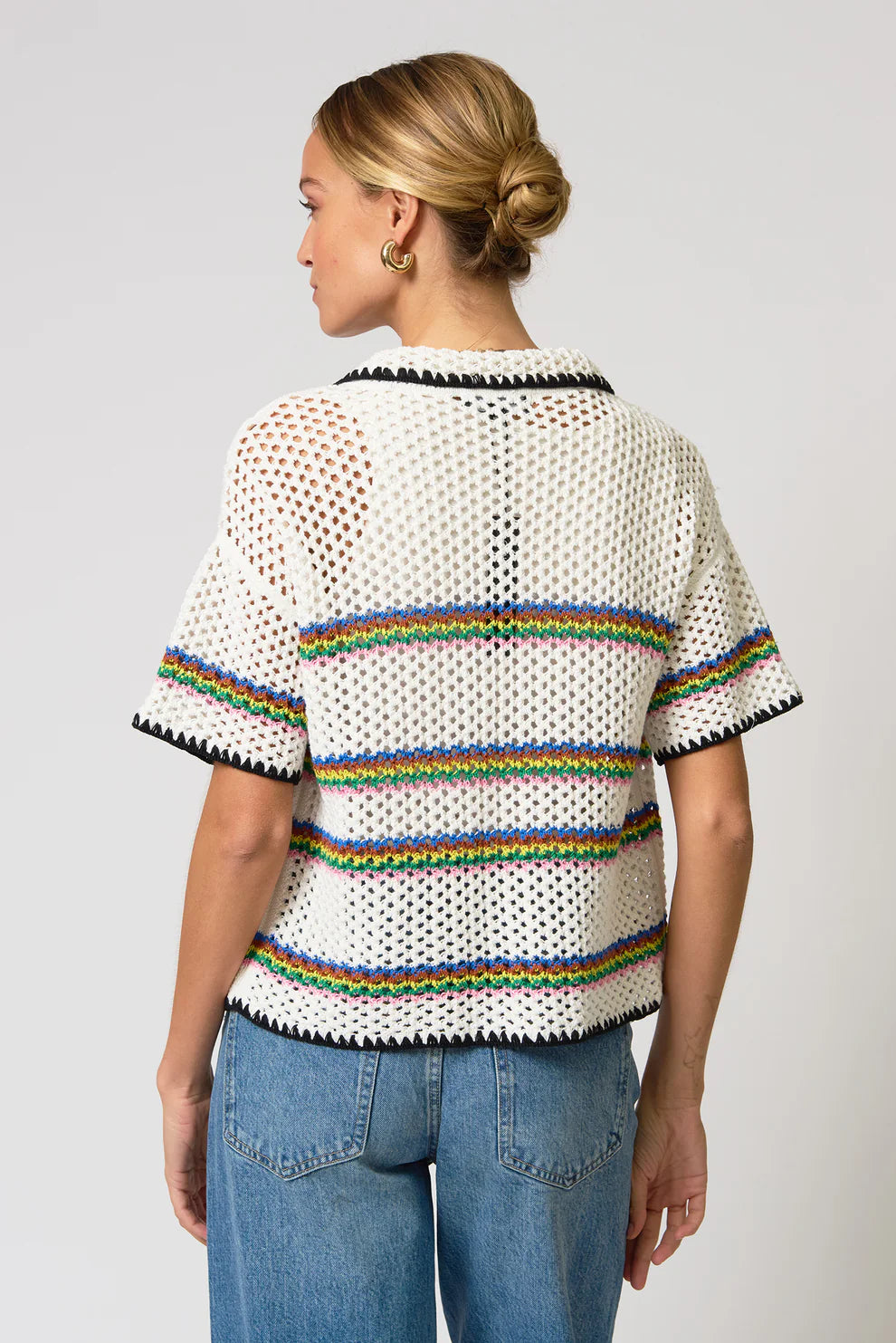 Person wearing a white knit top with rainbow trim on a plain background