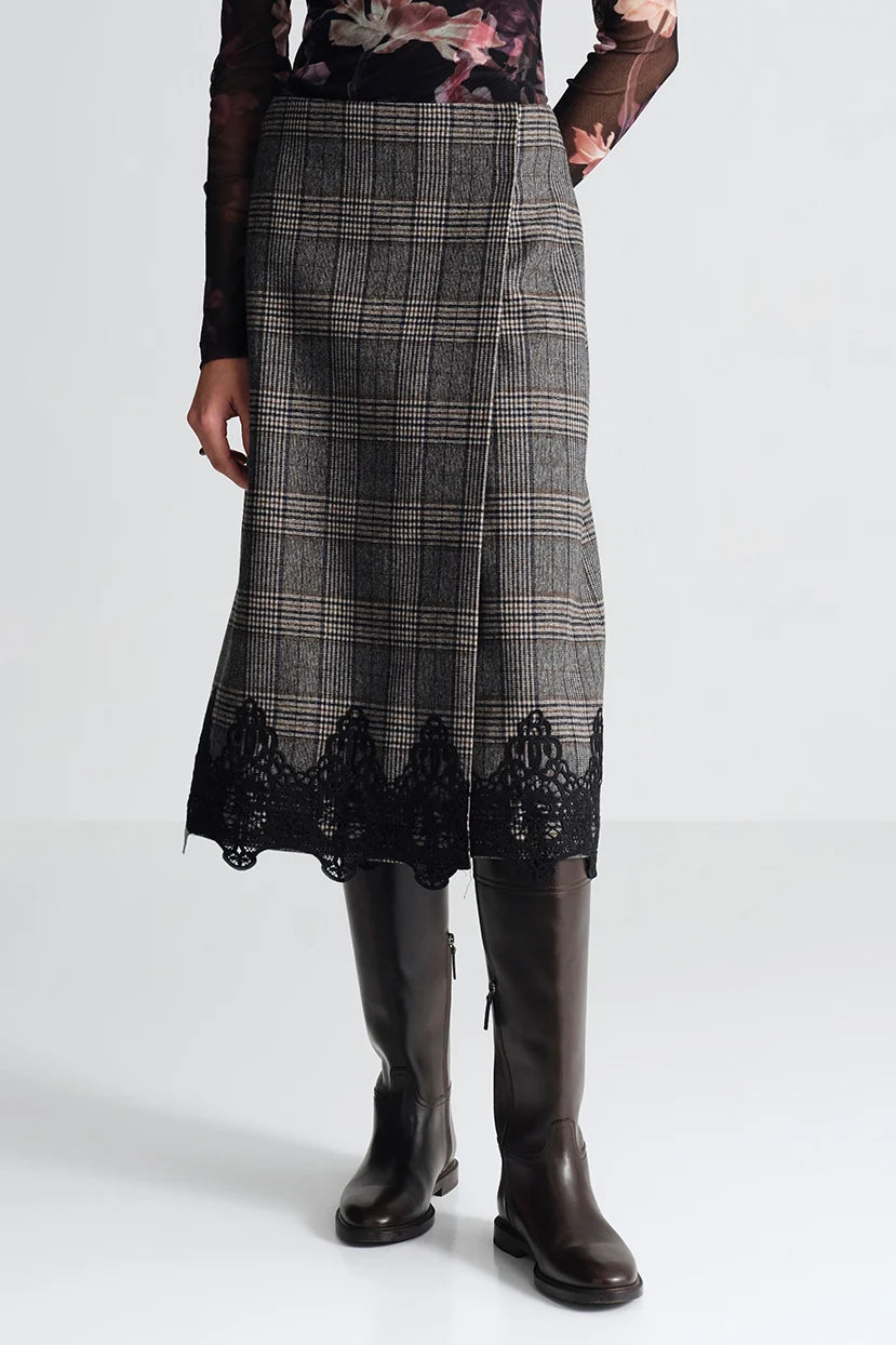 A model wearing a gray and black plaid midi skirt with a black lace hem, paired with dark brown leather knee-high boots and a sheer floral top.