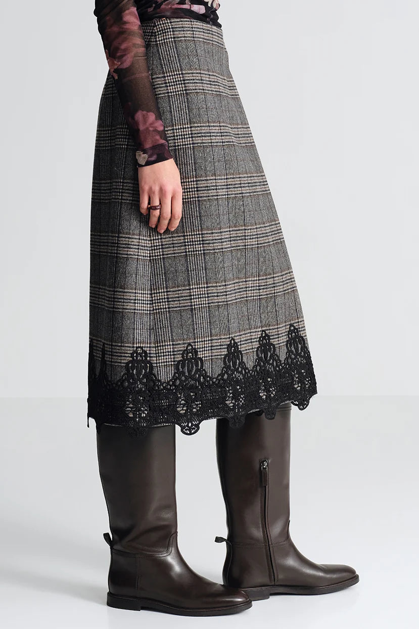 A gray and black plaid skirt with a black lace hem, worn by a model with dark brown leather knee-high boots against a light gray studio background.