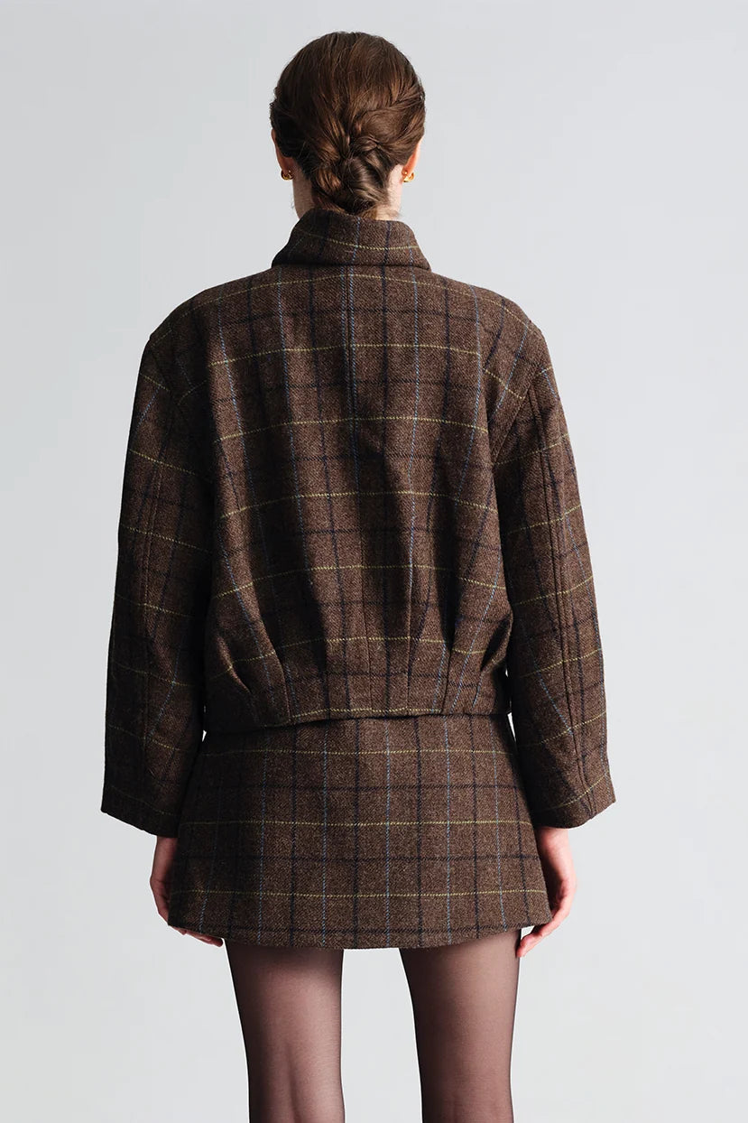 A model shown from the back wearing a brown plaid coat and matching skirt against a light gray studio background.
