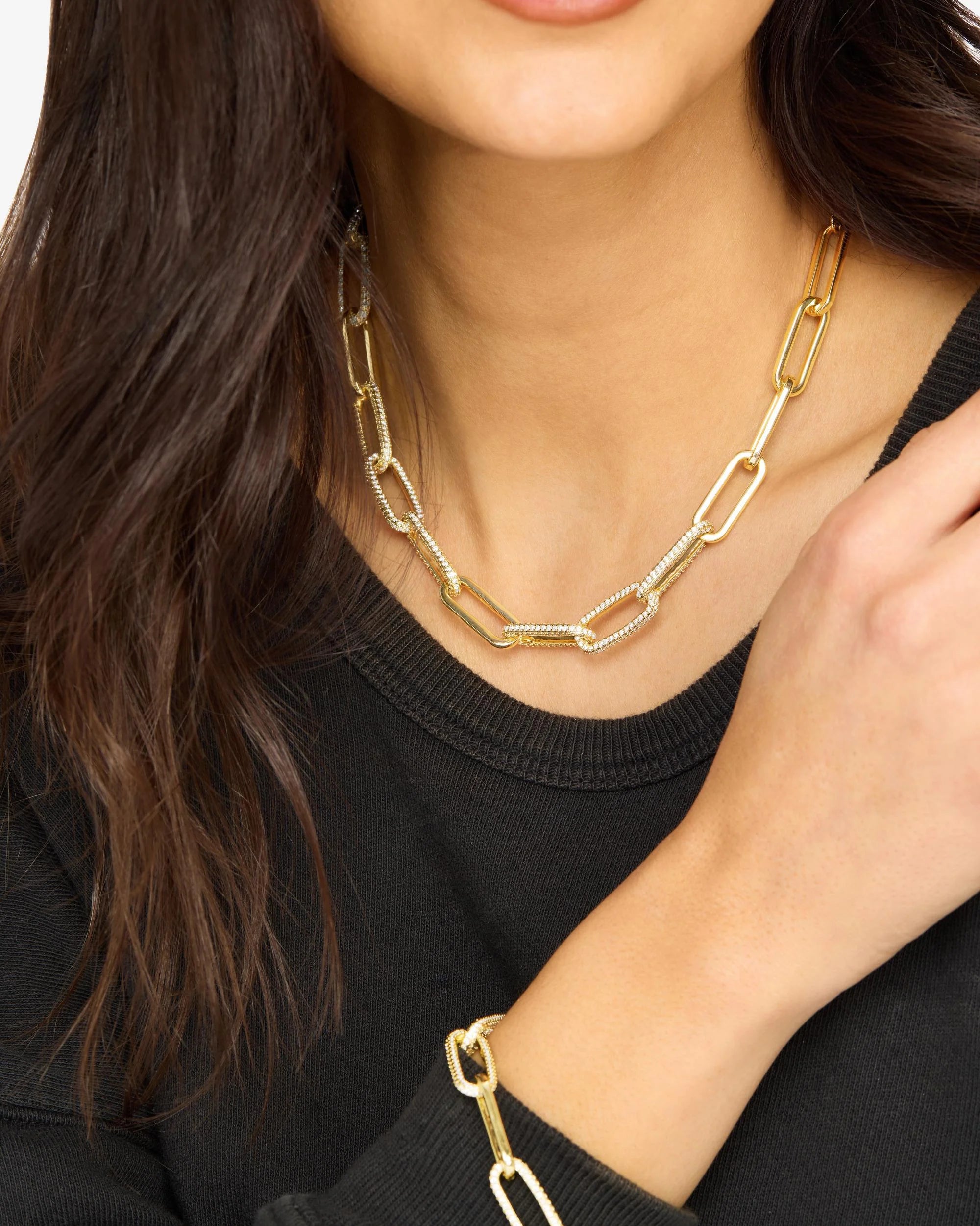 Gold chain necklace and bracelet on a person wearing a black top