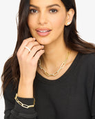 Woman wearing gold jewelry including a necklace, bracelet, and ring on a plain background