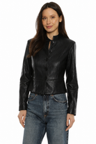 A woman modeling a black faux-leather cropped jacket with a stand-up collar and front buttons, paired with blue jeans, against a plain white background.