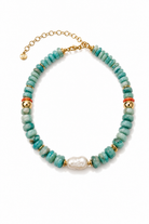 A beaded necklace featuring round turquoise-blue beads, gold spacer rings, two small orange-red beads, and a central irregular white pearl, displayed on a clean white background.