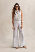 Woman wearing a striped sleeveless top and wide-leg pants on a beige background