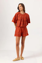 Woman wearing a rust-colored outfit with a top and shorts on a white background