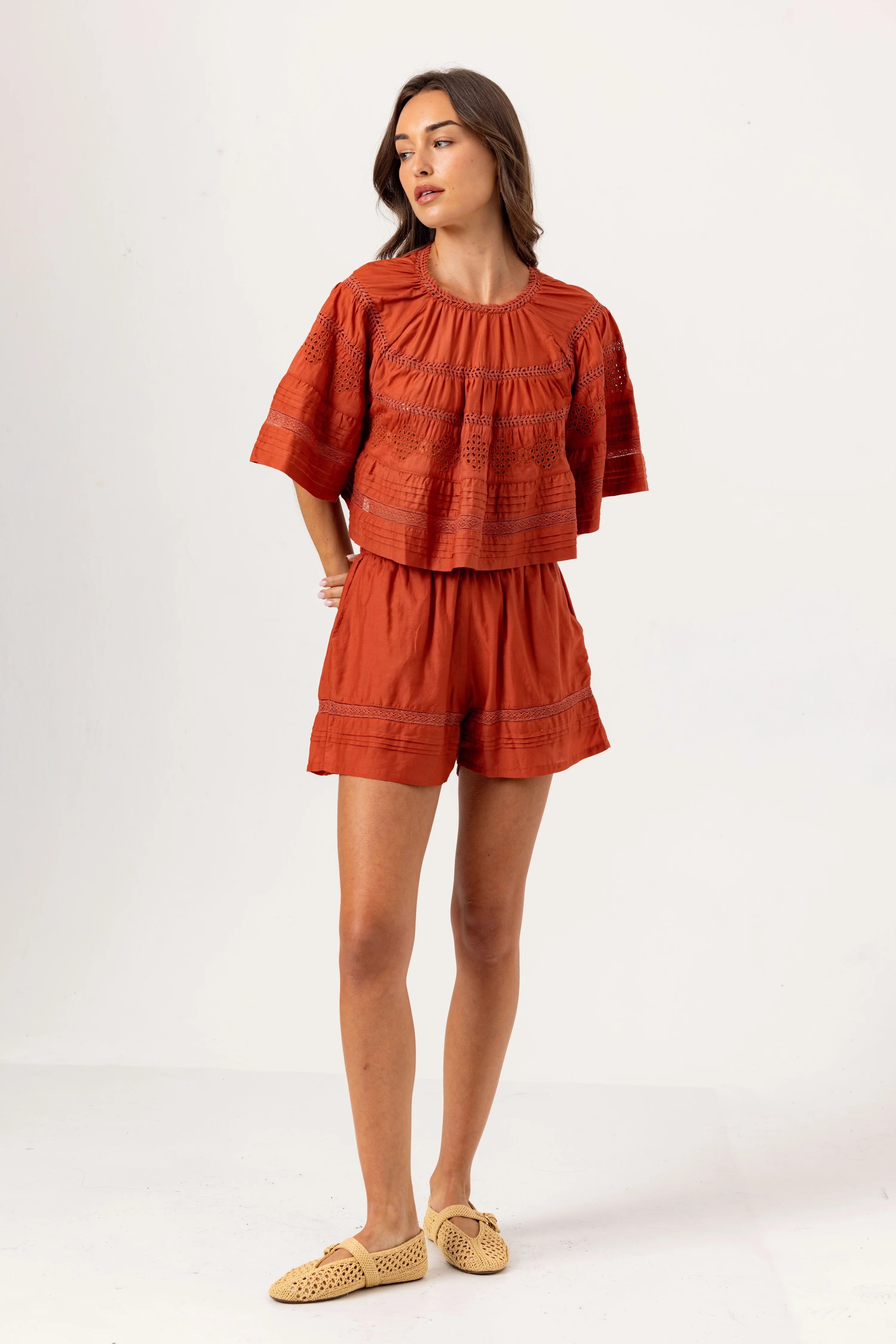 Woman wearing a rust-colored outfit with a top and shorts on a white background