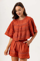 Woman wearing a rust-colored outfit with embroidered details on a white background