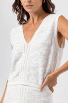 Woman wearing a white sleeveless top with a textured pattern on a plain background