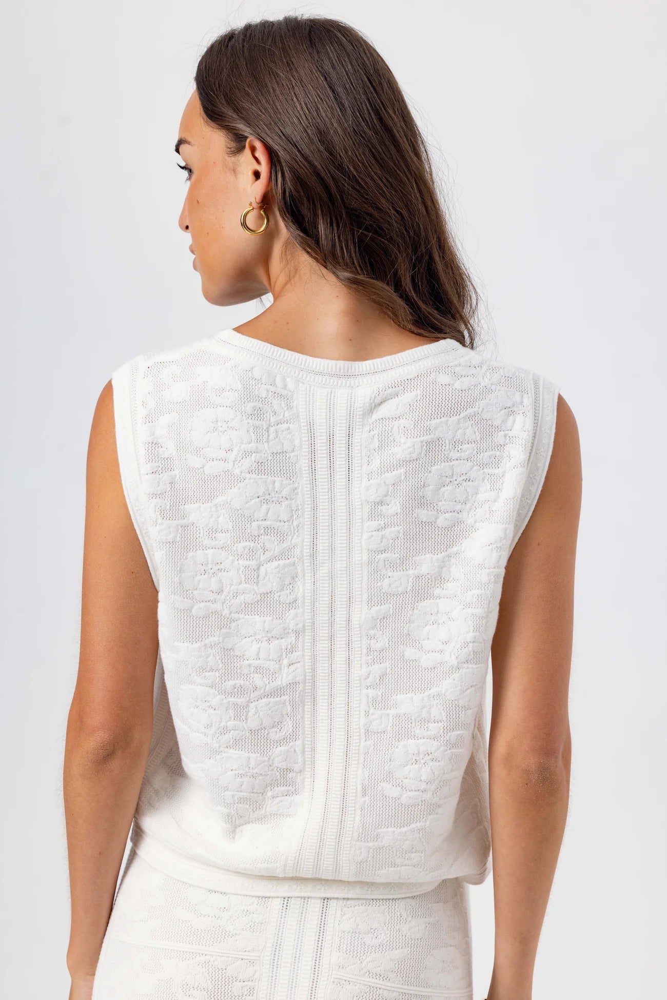 Woman wearing a white sleeveless top with intricate detailing on a plain background