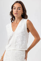 Woman wearing a white sleeveless top against a plain background