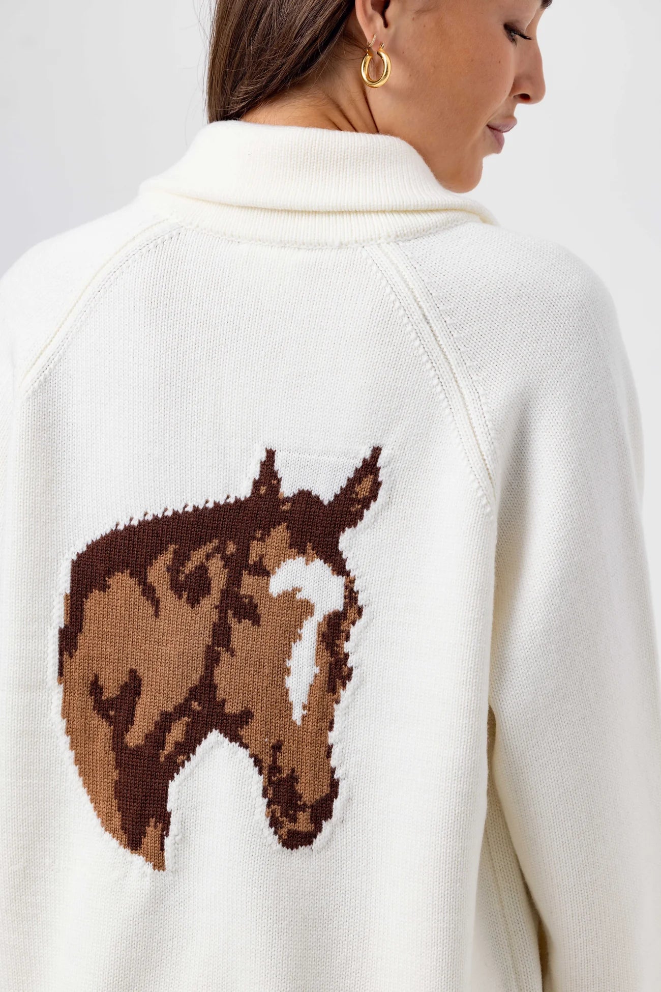 White sweater with a brown horse design on the back, worn by a person.