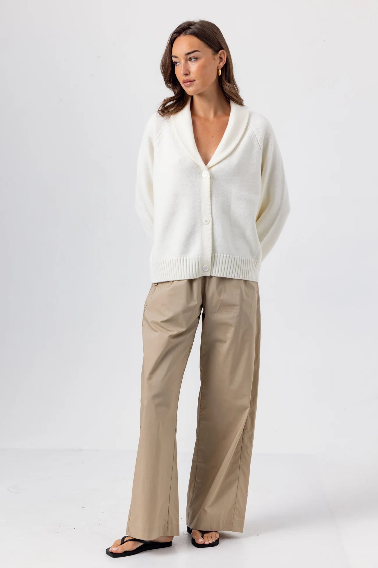 Woman wearing a white sweater and beige pants on a white background