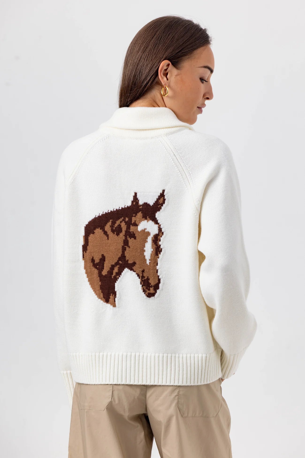 Person wearing a white sweater with a horse design on the back against a light gray background