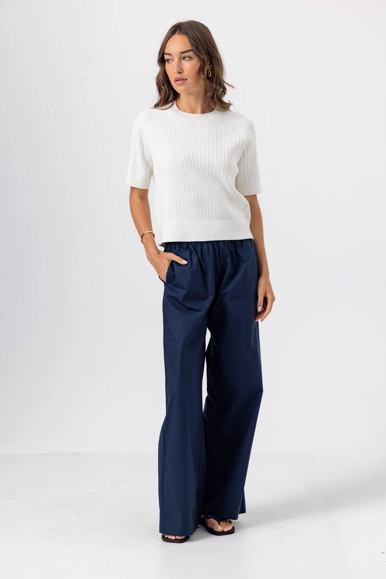 Woman wearing a white sweater and navy pants on a white background