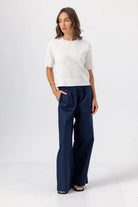 Woman wearing a white sweater and navy pants on a white background