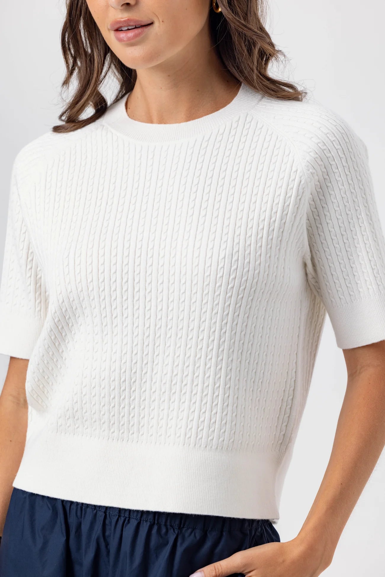 Woman wearing a white textured sweater with navy pants on a light gray background