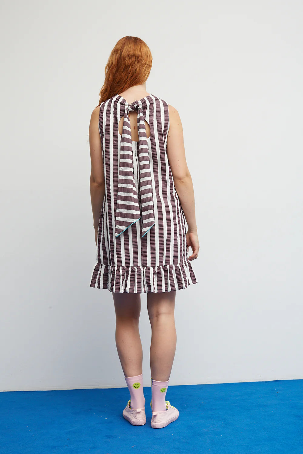 Woman wearing a striped dress with a blue floor and white wall background