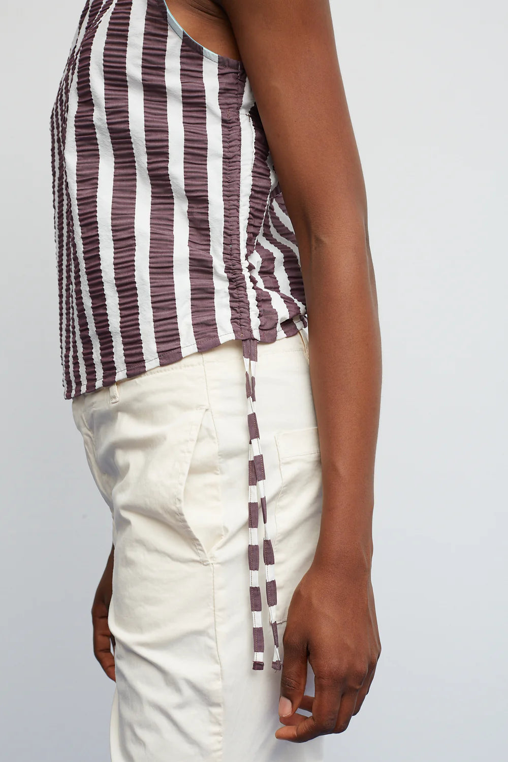 Person wearing a striped tank top and white pants on a plain background