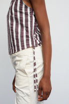 Person wearing a striped tank top and white pants on a plain background