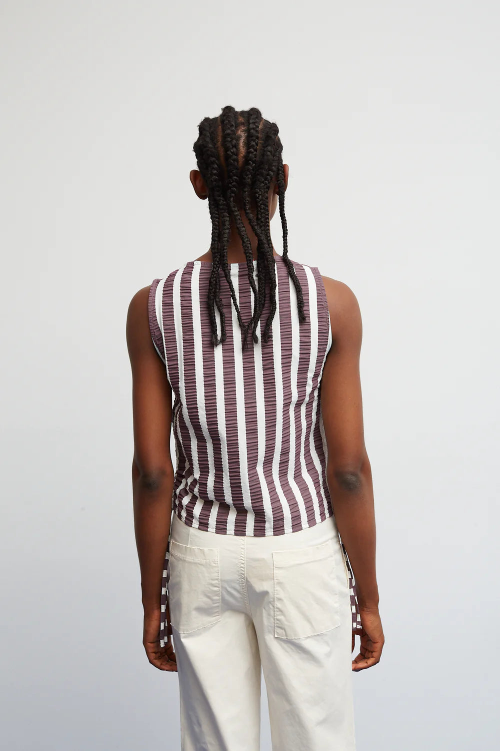Person wearing a sleeveless striped shirt and white pants on a plain background