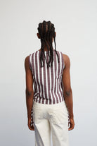 Person wearing a sleeveless striped shirt and white pants on a plain background