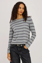Woman wearing a gray and blue striped sweater with black jeans on a plain background