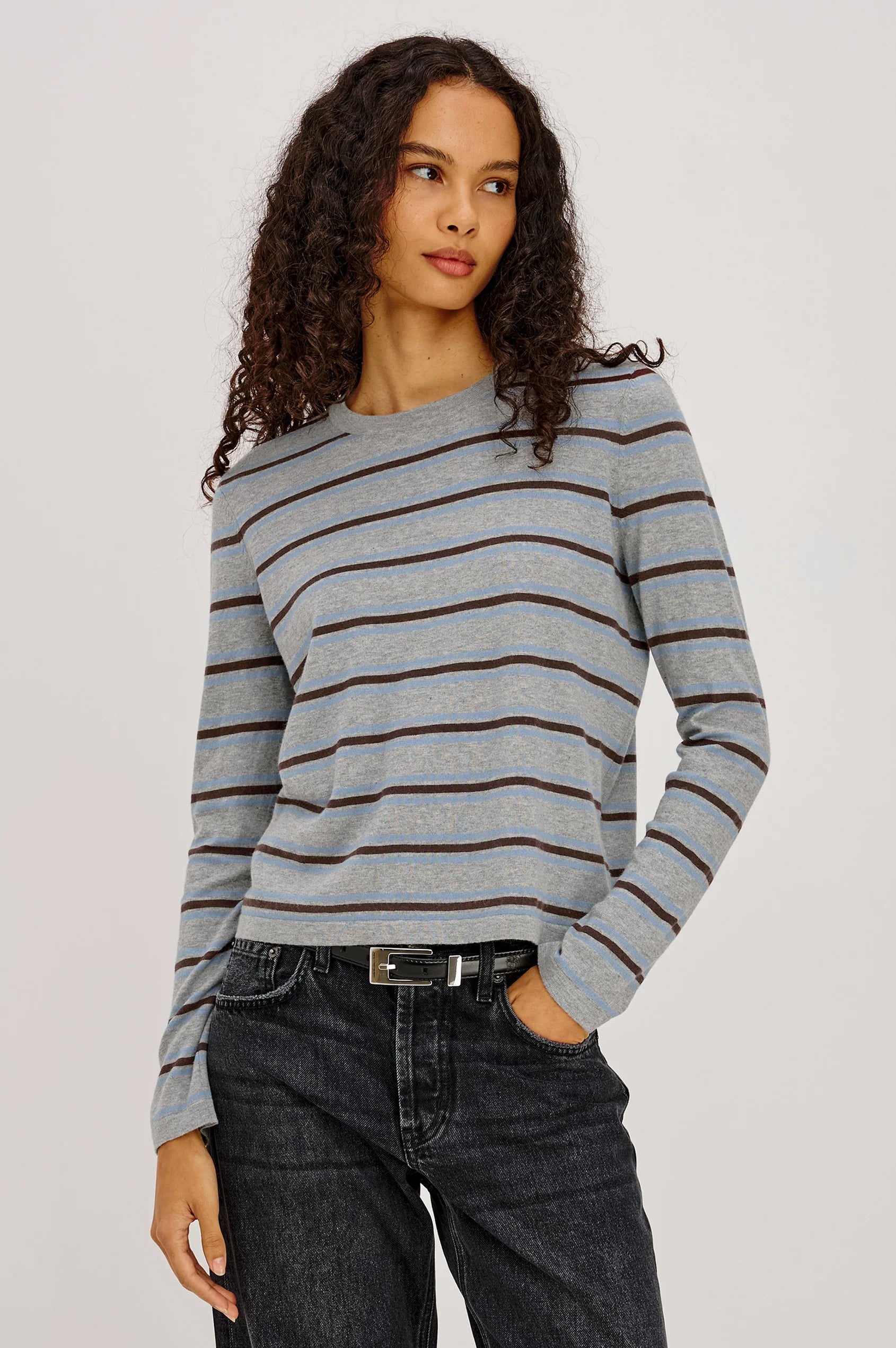 Woman wearing a gray and blue striped sweater with black jeans on a plain background