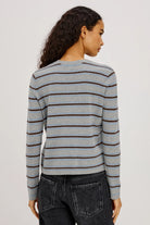 Woman wearing a gray and blue striped sweater with black jeans on a plain background from the back view.