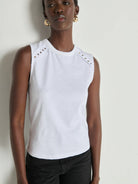 Woman wearing a white sleeveless top with cut-out details against a plain background