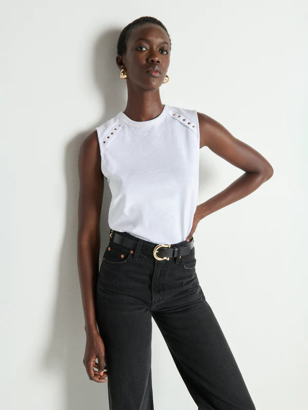 Woman wearing a white sleeveless top with cut-out details and black high-waisted jeans against a white background