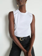 Person wearing a white sleeveless top with cut-out shoulders and black pants against a light background