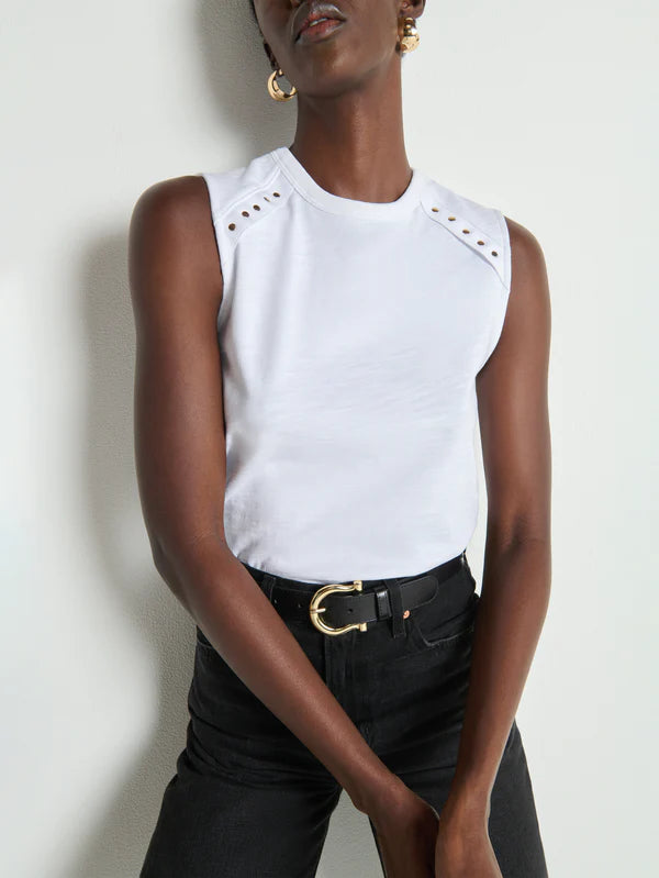 Person wearing a white sleeveless top with cut-out shoulders and black pants against a light background