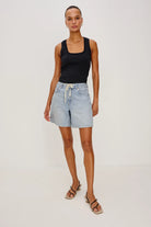 Woman wearing a black tank top and light blue denim shorts on a white background