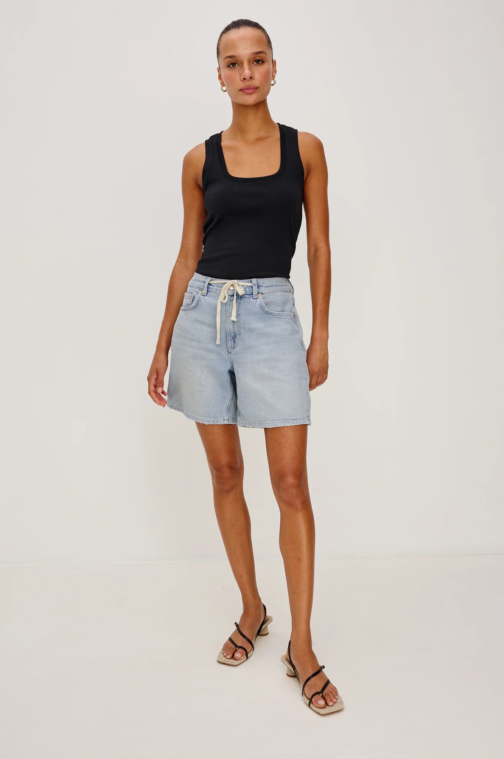 Woman wearing a black tank top and light blue denim shorts on a white background
