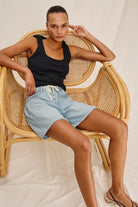 Woman sitting on a wicker chair wearing a black tank top and light blue denim shorts.