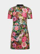 A short-sleeve mock-neck dress featuring a vibrant, dense floral print with pink, green, orange, and yellow flowers on a dark background, shown against a plain off-white studio backdrop.