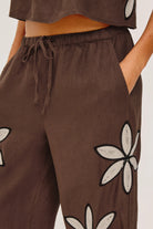 Brown pants with floral patterns worn by a person on a neutral background