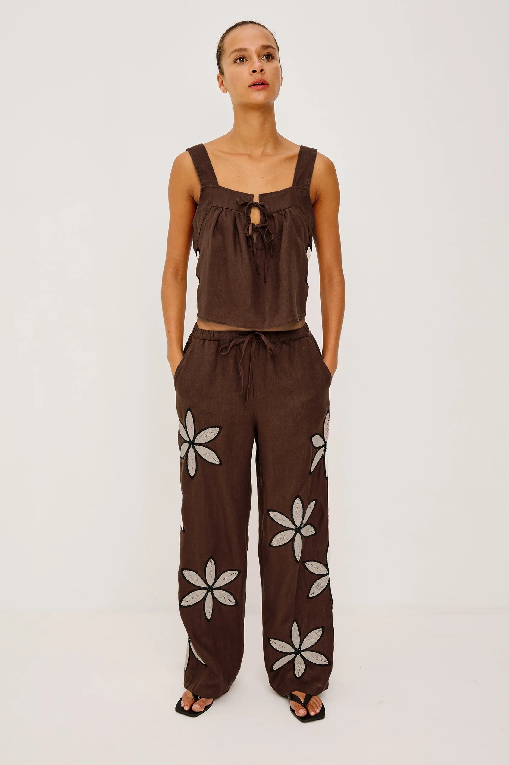 Woman wearing a brown sleeveless top and wide-leg pants with floral patterns on a white background