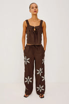 Woman wearing a brown sleeveless top and wide-leg pants with floral patterns on a white background
