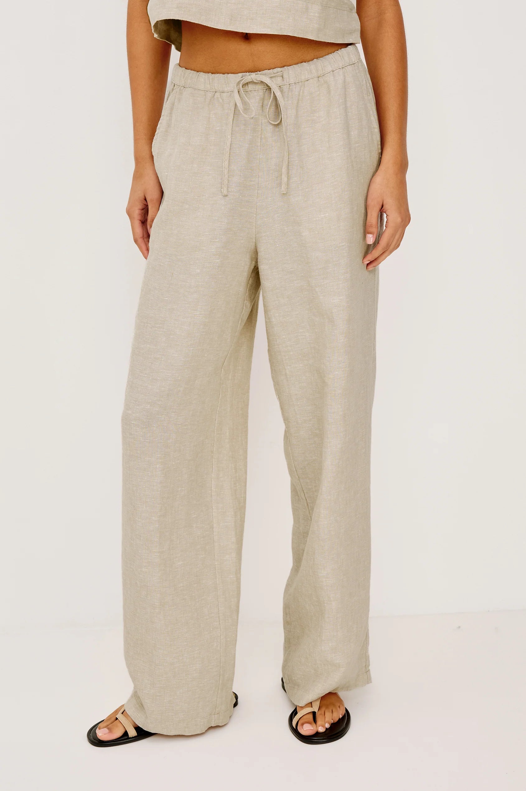 Beige linen pants worn by a person on a white background