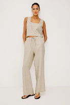Woman wearing a beige sleeveless top and wide-leg pants on a white background