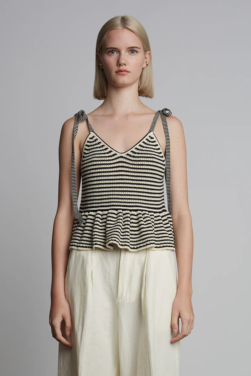 Woman wearing a black and white striped tank top with beige pants on a gray background